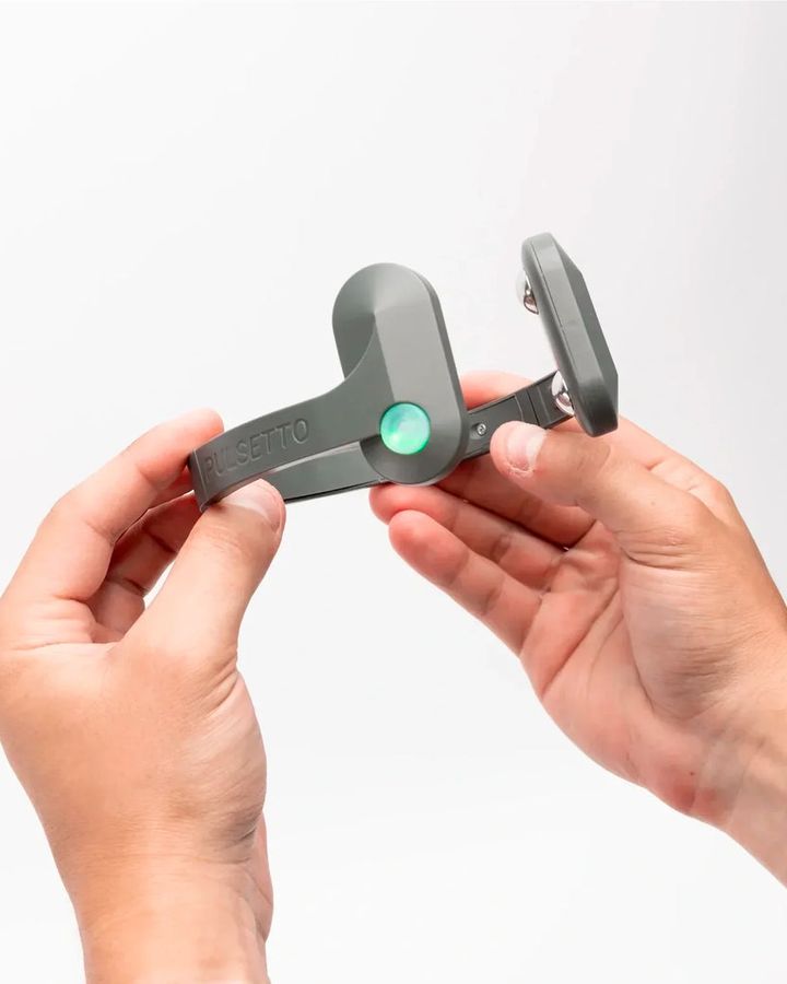 Two hands holding the Pulsetto Lite open, showing the central hinge and the two stimulation pads